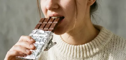 Eine Frau beisst in eine Tafel Schokolade (KI-generiertes Stockfoto)